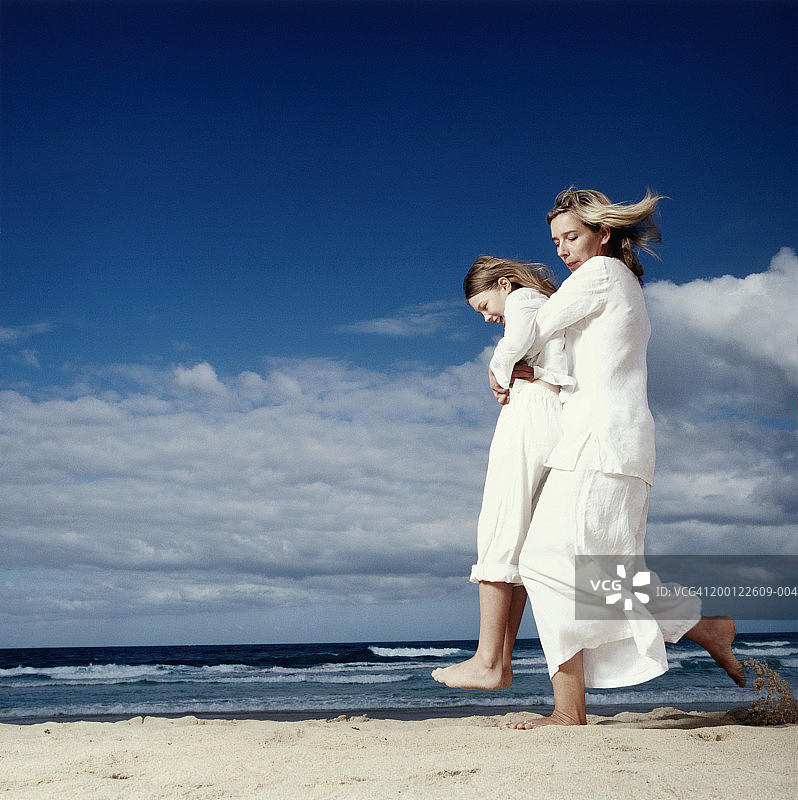母亲在海滩上背着女儿（8-10岁），侧视图图片素材