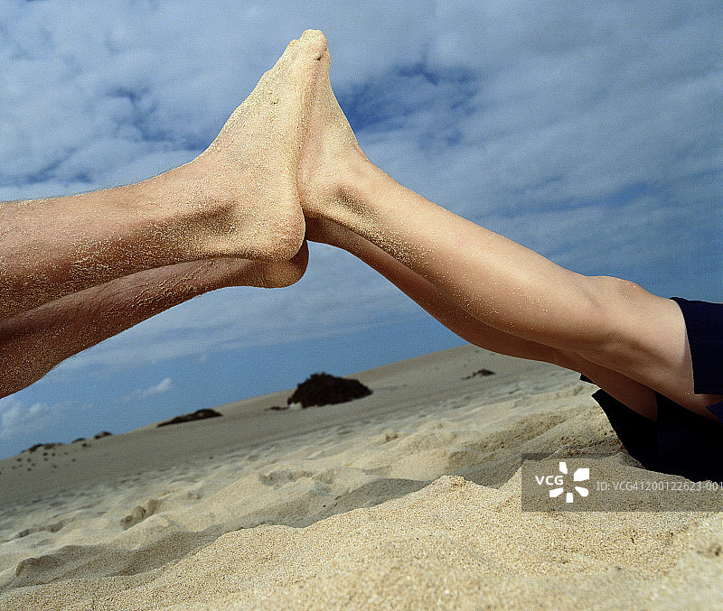 男人和男孩（6-8岁）在海滩上脚碰脚，低角度拍摄图片素材