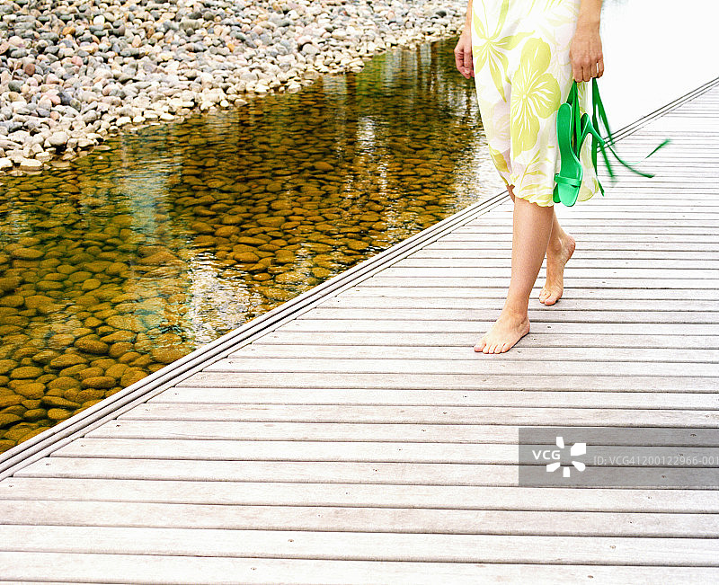 女人走在水景旁的木板路上，低角度拍摄图片素材
