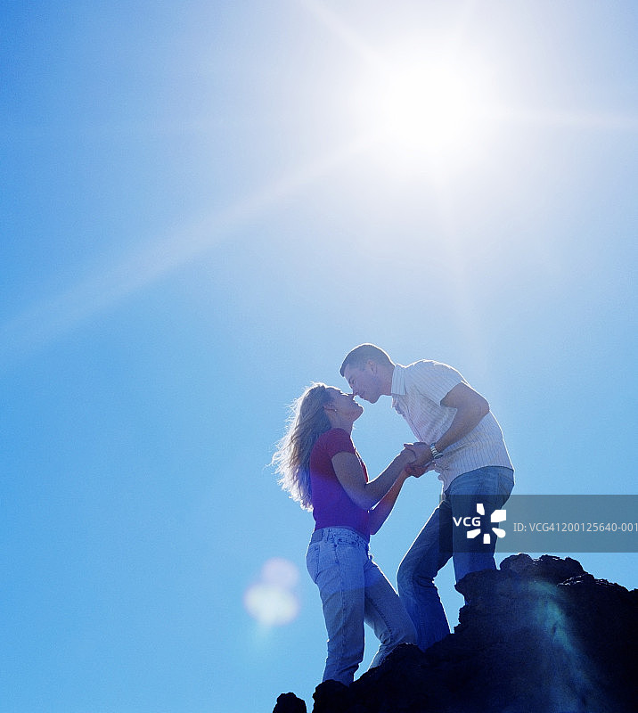 在岩石地形上的情侣，男子弯腰亲吻女子图片素材