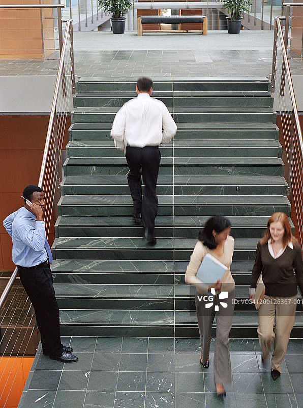 职场人士在楼梯上，男子使用手机，高角度拍摄图片素材