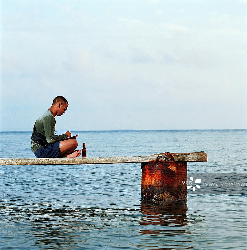 年轻男人坐在码头上看书，侧视图图片素材