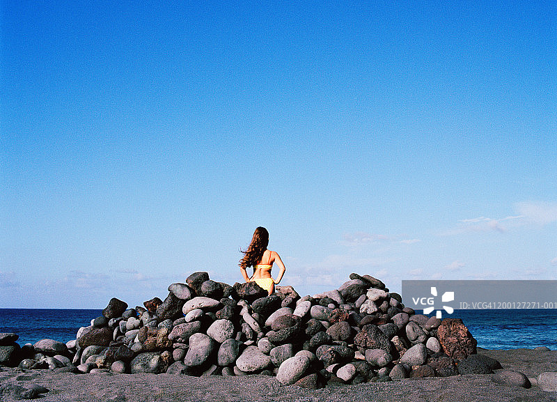 后视图：6-8岁女孩站在面向大海的岩石堆上图片素材