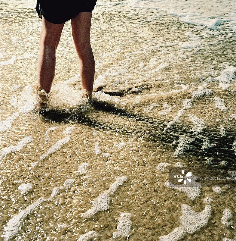 小女孩站在海滩上，海浪冲刷着她的脚图片素材