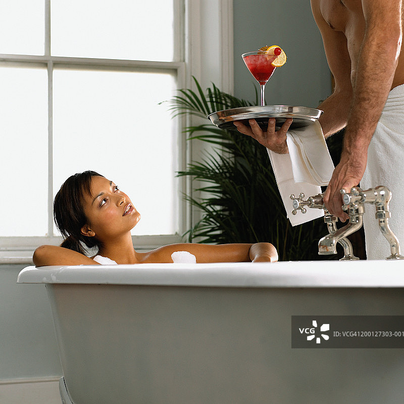 男人为在泡泡浴中放松的女人提供异国情调的饮品图片素材