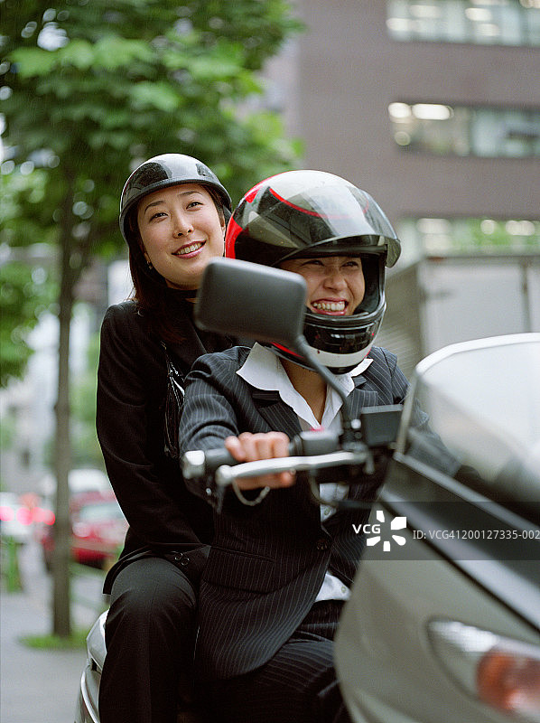 两位女商人骑着摩托车，欢笑着图片素材