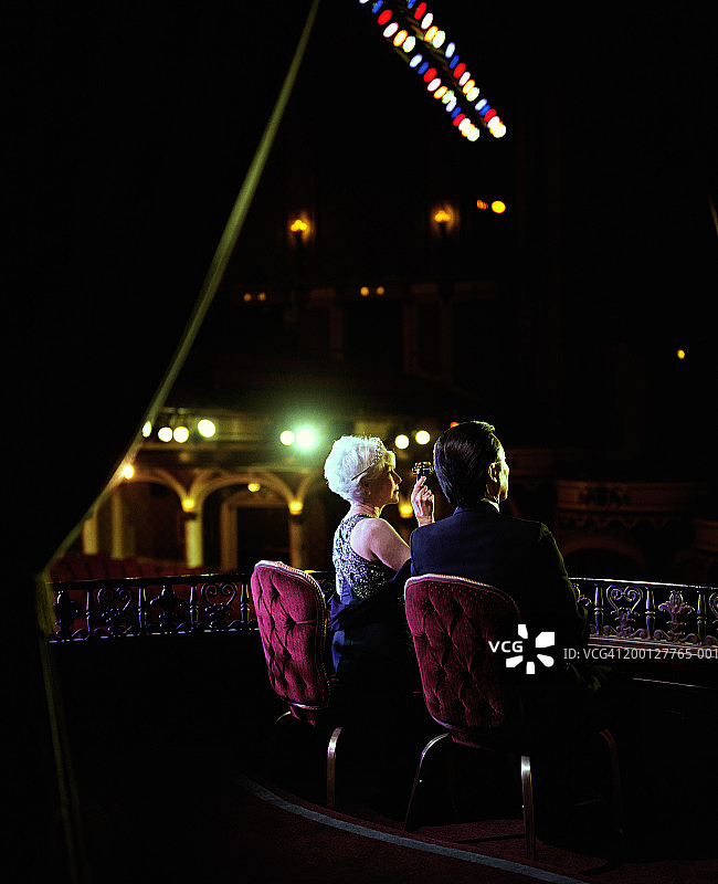 一对中年夫妇坐在剧院的包厢里，女人正在使用歌剧镜图片素材