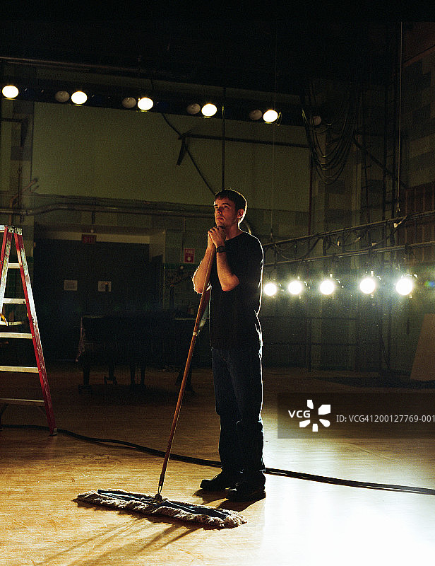 站在空旷剧院舞台上手扶拖把的年轻男人图片素材