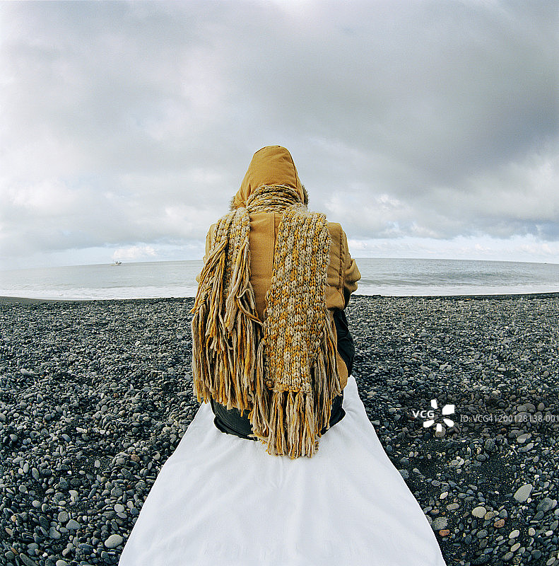 穿着冬装坐在卵石滩上的男人，背影图片素材