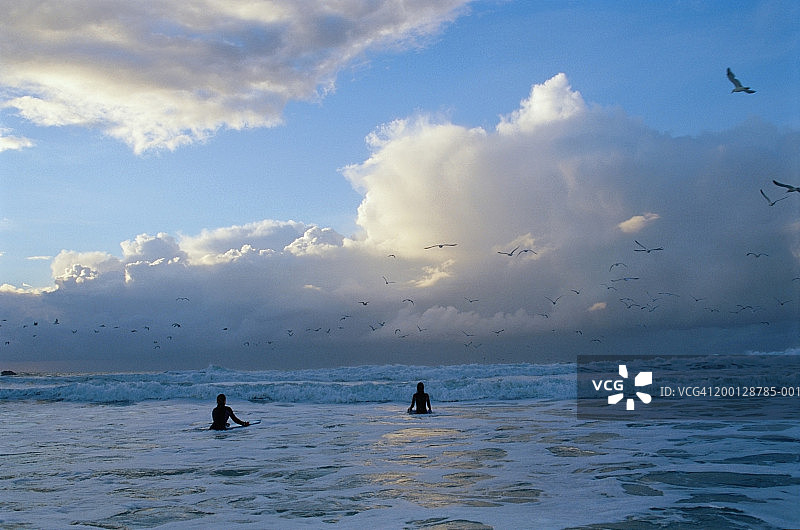 两个女孩(11-13岁)在海边拿着趴板，剪影图片素材