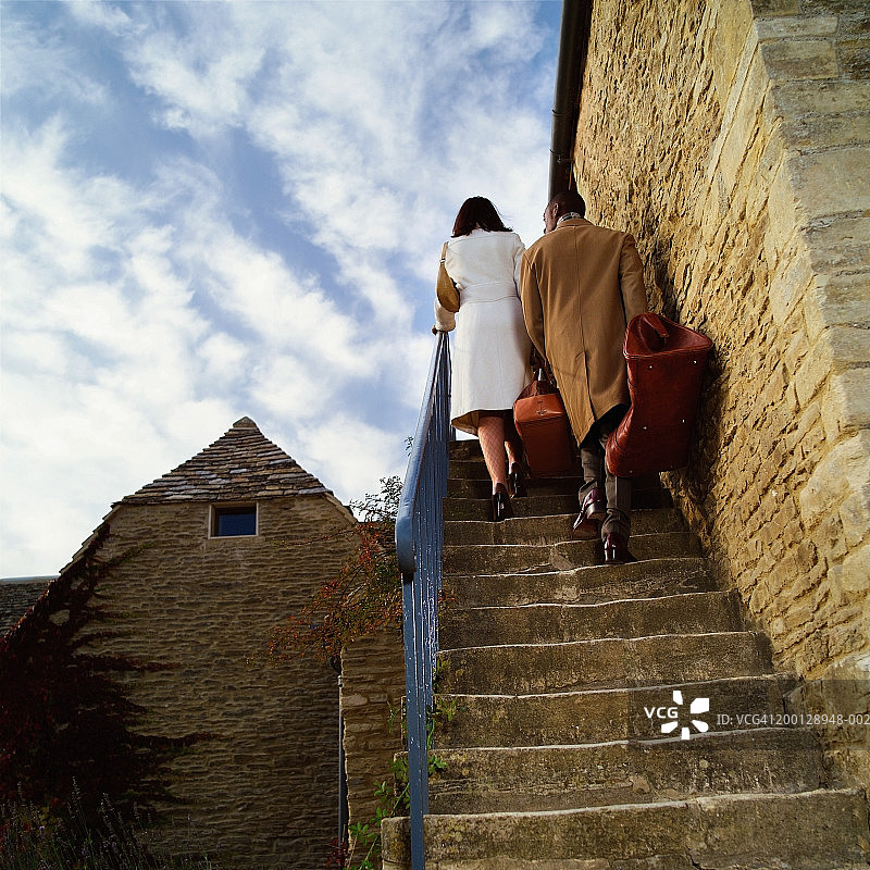 情侣扛着行李箱走上房子一侧的台阶，后视图图片素材
