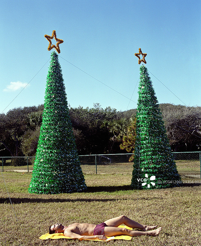 在圣诞树前晒日光浴的男人，侧视图图片素材
