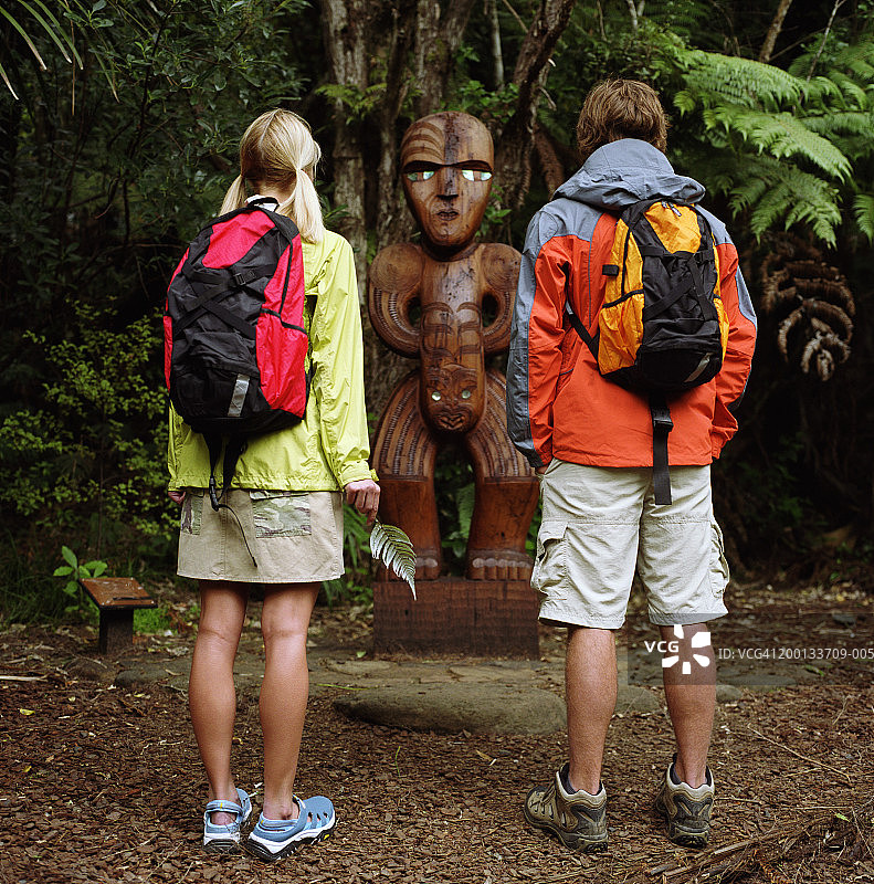 年轻情侣观看雕刻品，女子手持银蕨，后视图图片素材