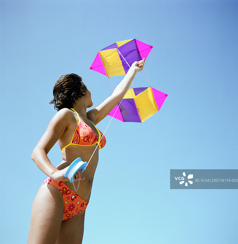 穿着泳衣拿着风筝线的年轻女人（低角度）图片素材