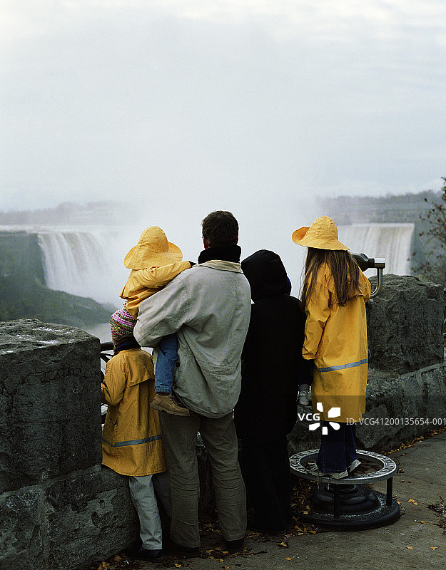 一家人观看瀑布，儿童（2-10岁）穿着雨衣，后视图图片素材