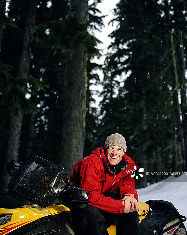 男子穿着冬装靠在雪地摩托上，笑着图片素材
