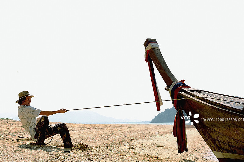 年轻男人在海滩上拉着连接长尾船的绳索图片素材