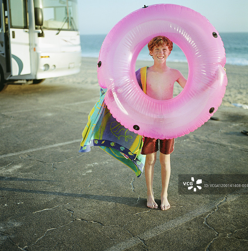 穿泳衣的男孩（9-11岁）拿着游泳圈站在海滩旁图片素材