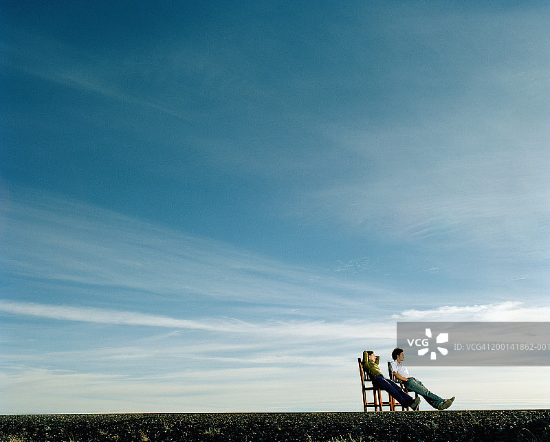 年轻夫妇坐在路边的椅子上，侧视图图片素材