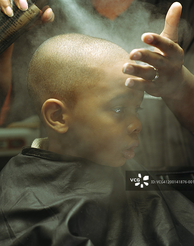 理发师在男孩（2-4岁）的头上喷洒光泽剂，特写图片素材