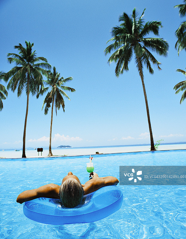 在泳池里坐在充气筏上的青少年男孩，后视图图片素材