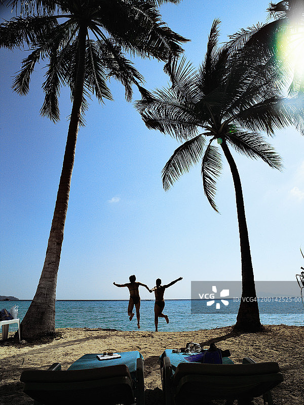 情侣在棕榈树间奔向大海，后视图图片素材