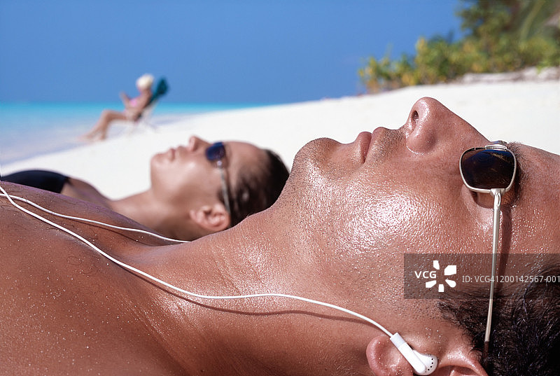 夫妇在海滩上晒日光浴（焦点在戴着耳机的男人身上）图片素材
