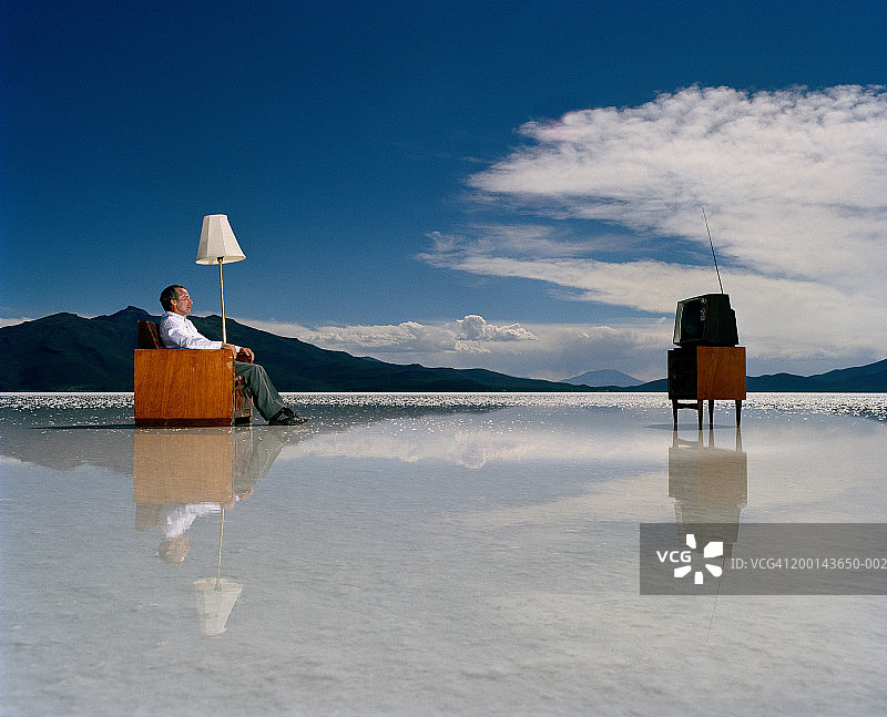 中年男人在盐滩上看电视，侧面视角图片素材