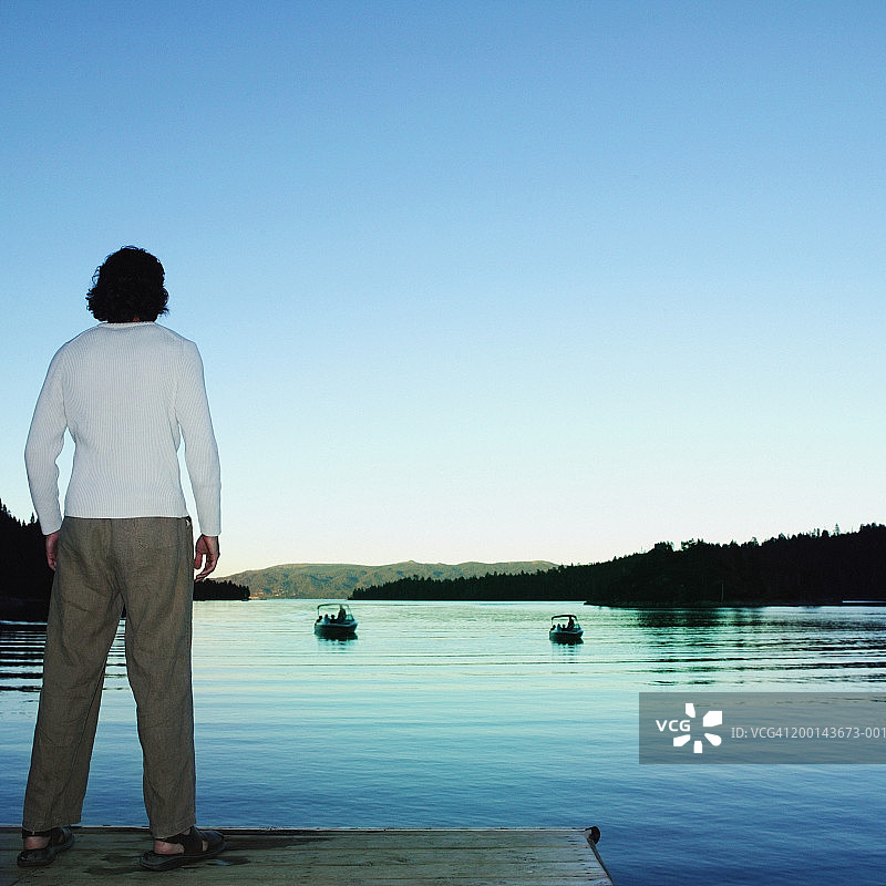 在码头看船和日落的年轻男子（后视图）图片素材