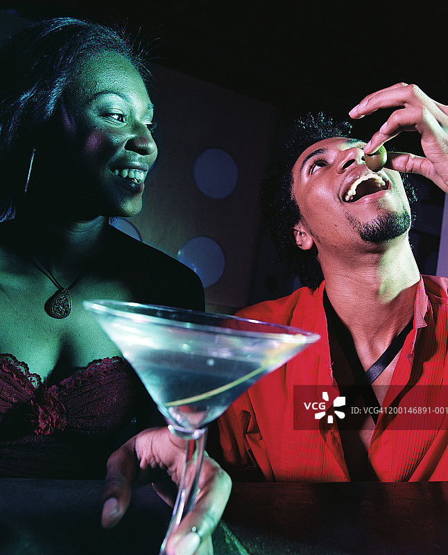 年轻女子在夜总会观看年轻男子吃橄榄，特写图片素材