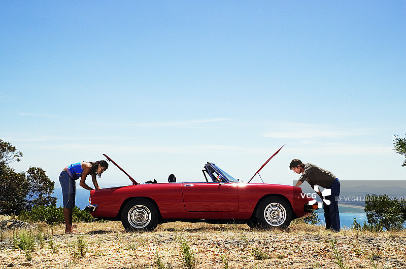情侣在敞篷车旁查看后备箱和引擎盖（侧视图）图片素材