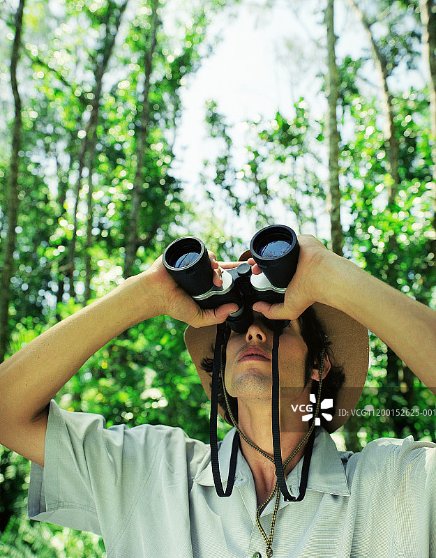 年轻男子在丛林中用双筒望远镜观察图片素材