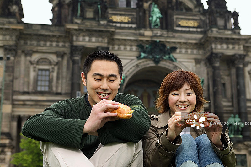 年轻情侣坐在地上吃面包卷，微笑图片素材