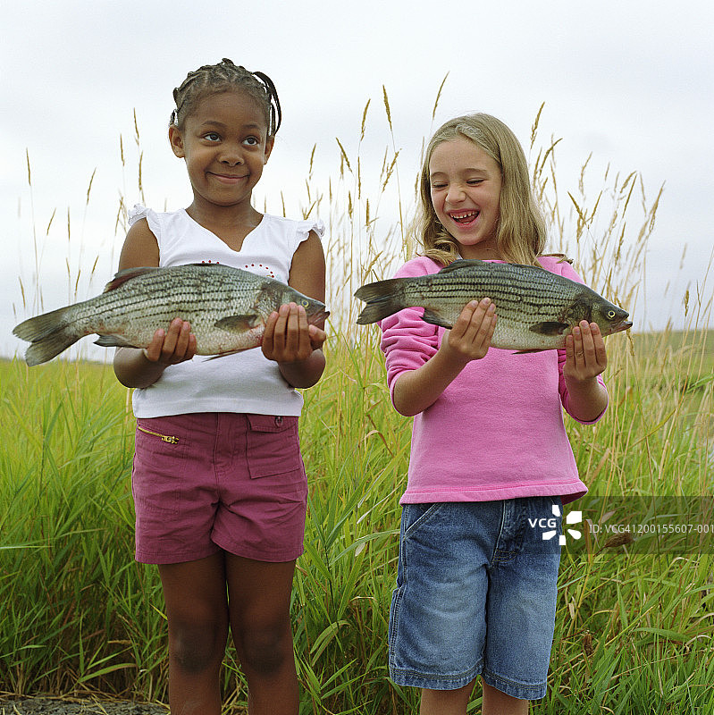 两个女孩（6-8岁）并排站立，拿着低音提琴，微笑着图片素材