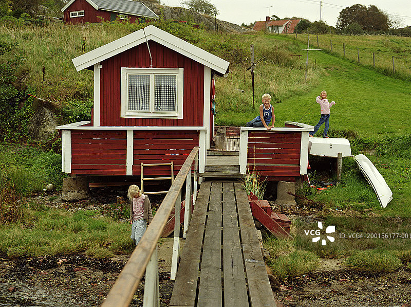 五到七岁的三个孩子在小屋和木板路旁玩耍图片素材