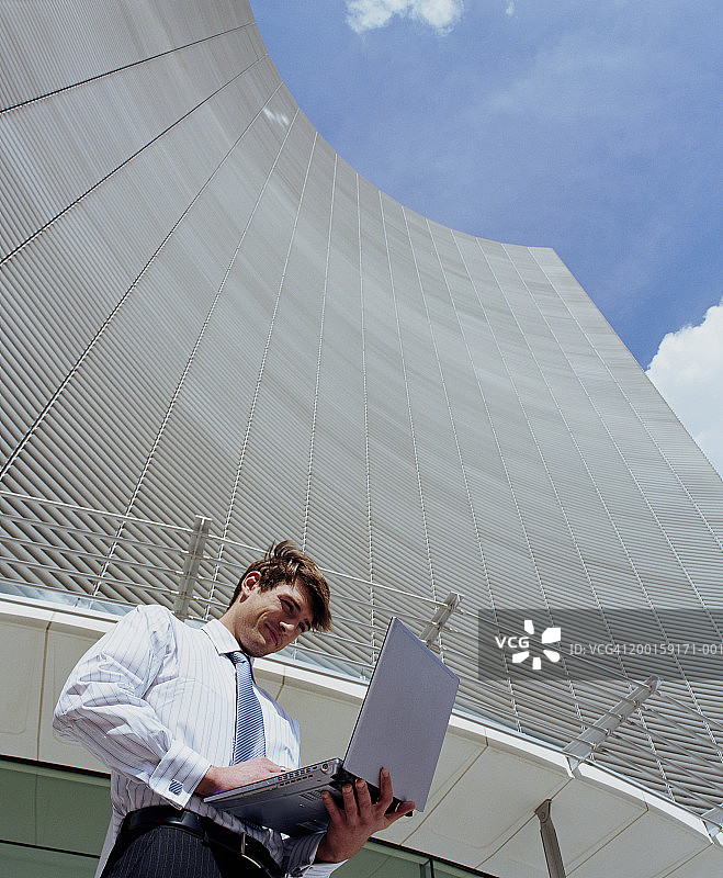 在办公楼外使用笔记本电脑的商务男士图片素材
