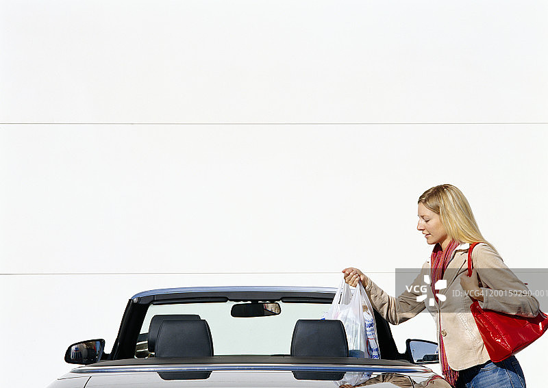 女性将购物袋放入敞篷车，侧视图图片素材
