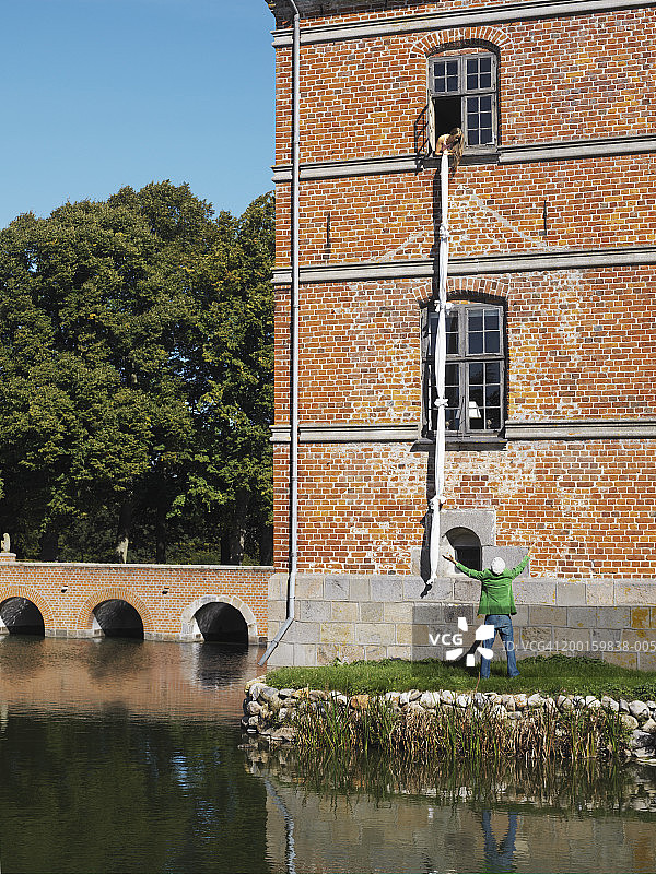 女人把打结的床单从窗户放给地面上的男人图片素材