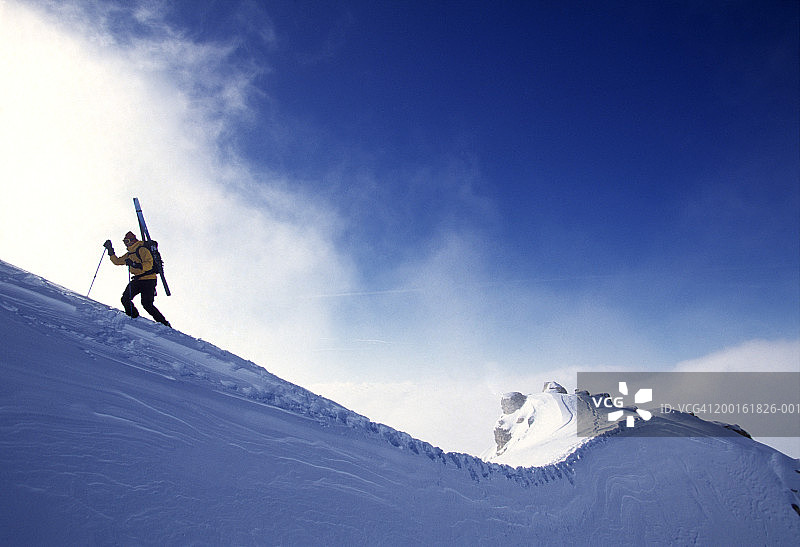滑雪者攀登雪脊，背包上绑着滑雪板图片素材