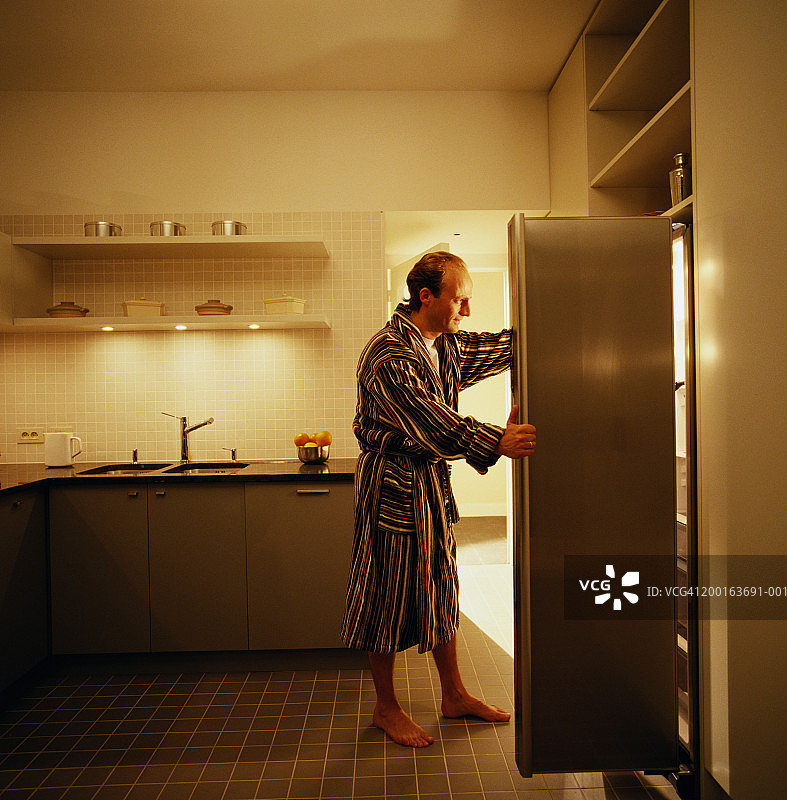 在厨房里的男人打开冰箱门，侧视图图片素材