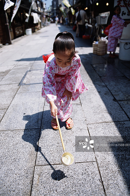 用勺子在人行道上浇水的小女孩图片素材