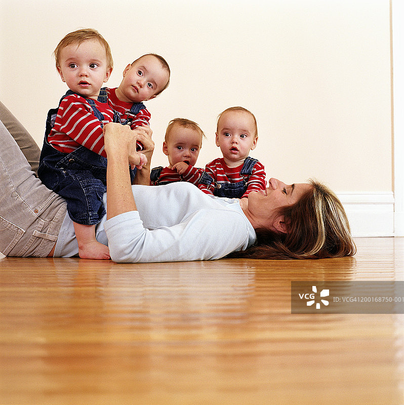 母亲和四胞胎宝宝（9-12个月大）躺在硬木地板上图片素材