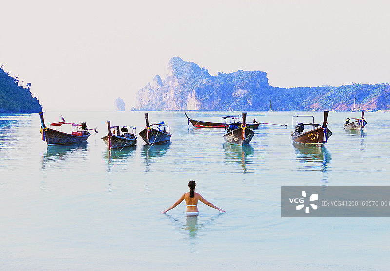 女人在海中涉水，前方有船只，后视图图片素材