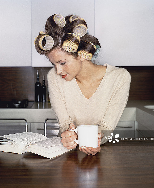 年轻女人在厨房里读书，头上卷着大发卷图片素材