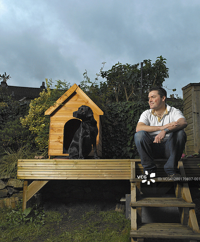 坐在花园狗窝外的狗，男人坐在附近的台阶上图片素材
