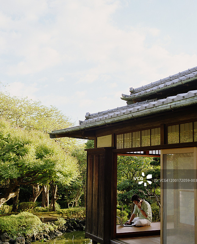 在房间里使用手机和笔记本电脑，俯瞰花园的年轻男人图片素材