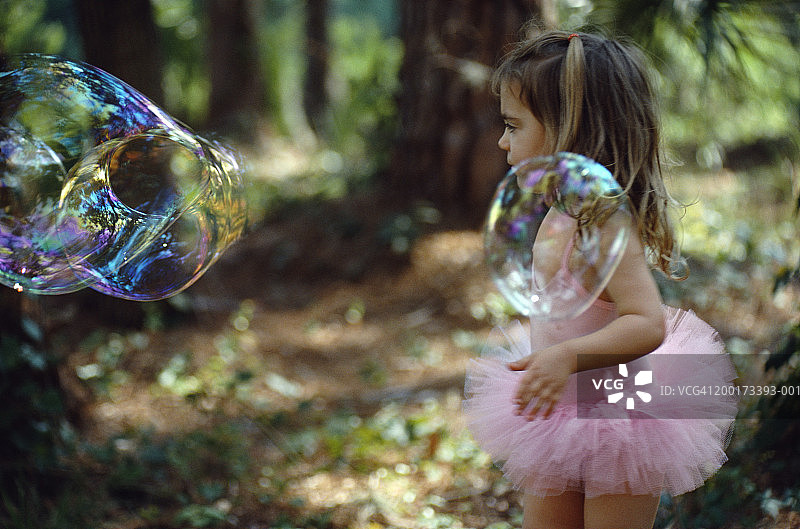 穿着芭蕾舞裙在林地里观看大泡泡的小女孩（2-4岁）图片素材