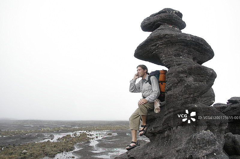 倚靠在岩石上使用手机的男人图片素材