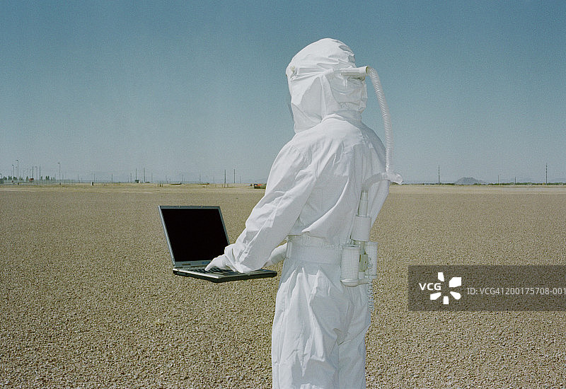 在沙漠中，戴防护装备使用悬浮笔记本电脑的男人（后视图）图片素材