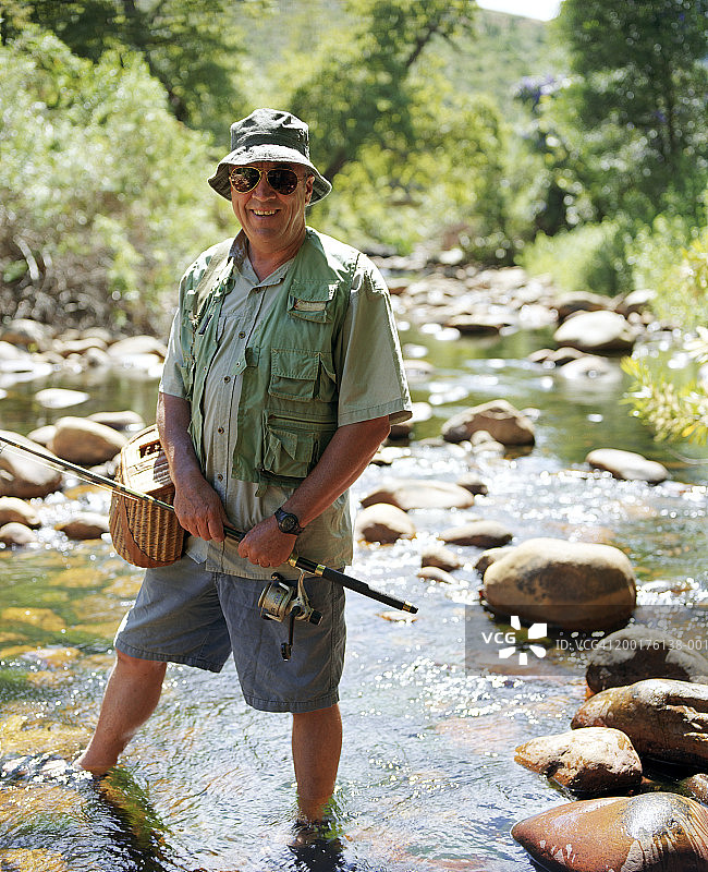 面带微笑，手持渔具在溪流中的中年男人肖像图片素材